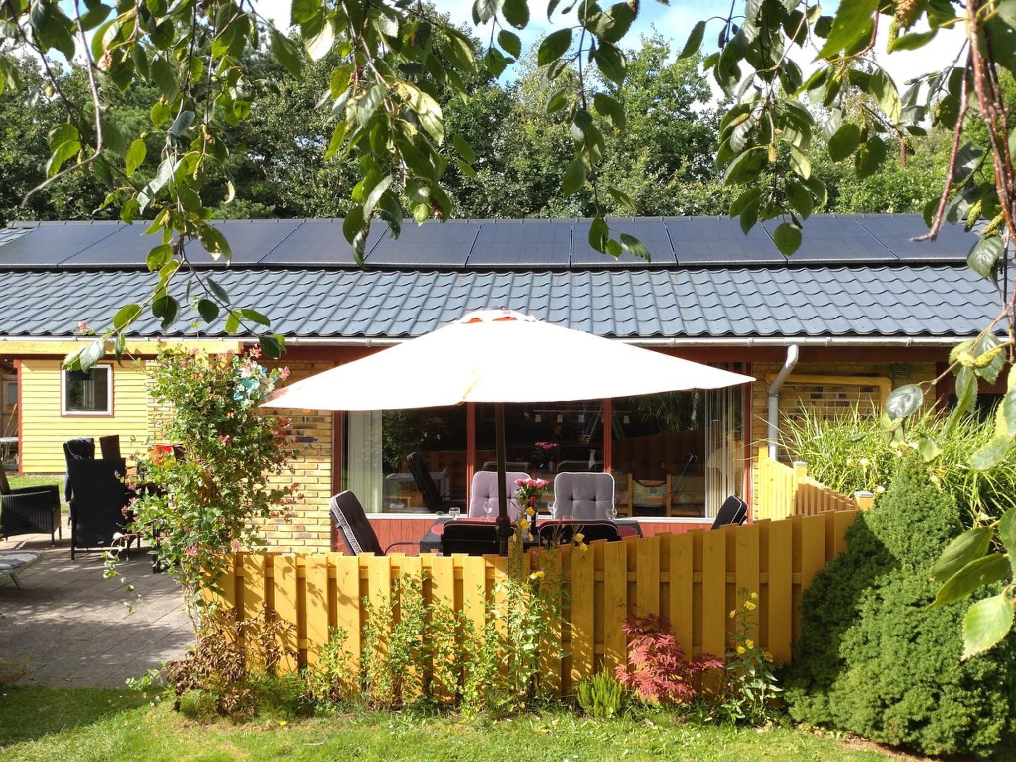 Un bâtiment jaune doté d’un patio couvert, avec des sièges en plein air et un grand parasol.