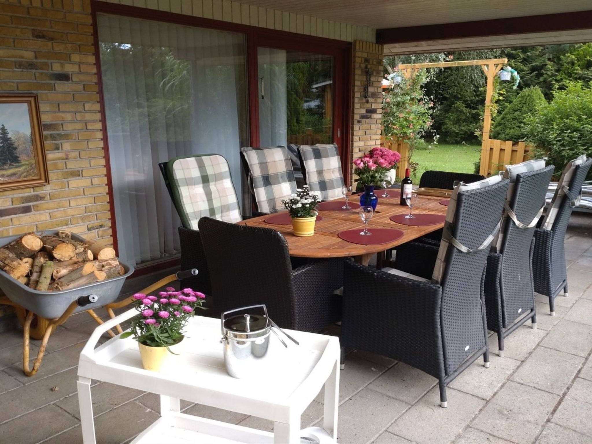 An outdoor patio with a round table, wicker chairs, and a white table with a flower pot.