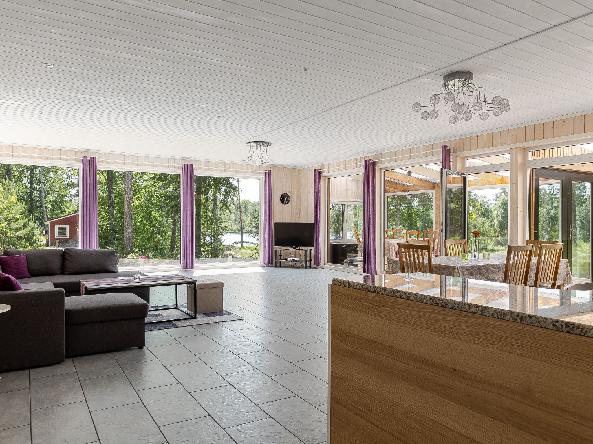 A spacious living area with a large window, a sofa, a coffee table, and a dining table with chairs.