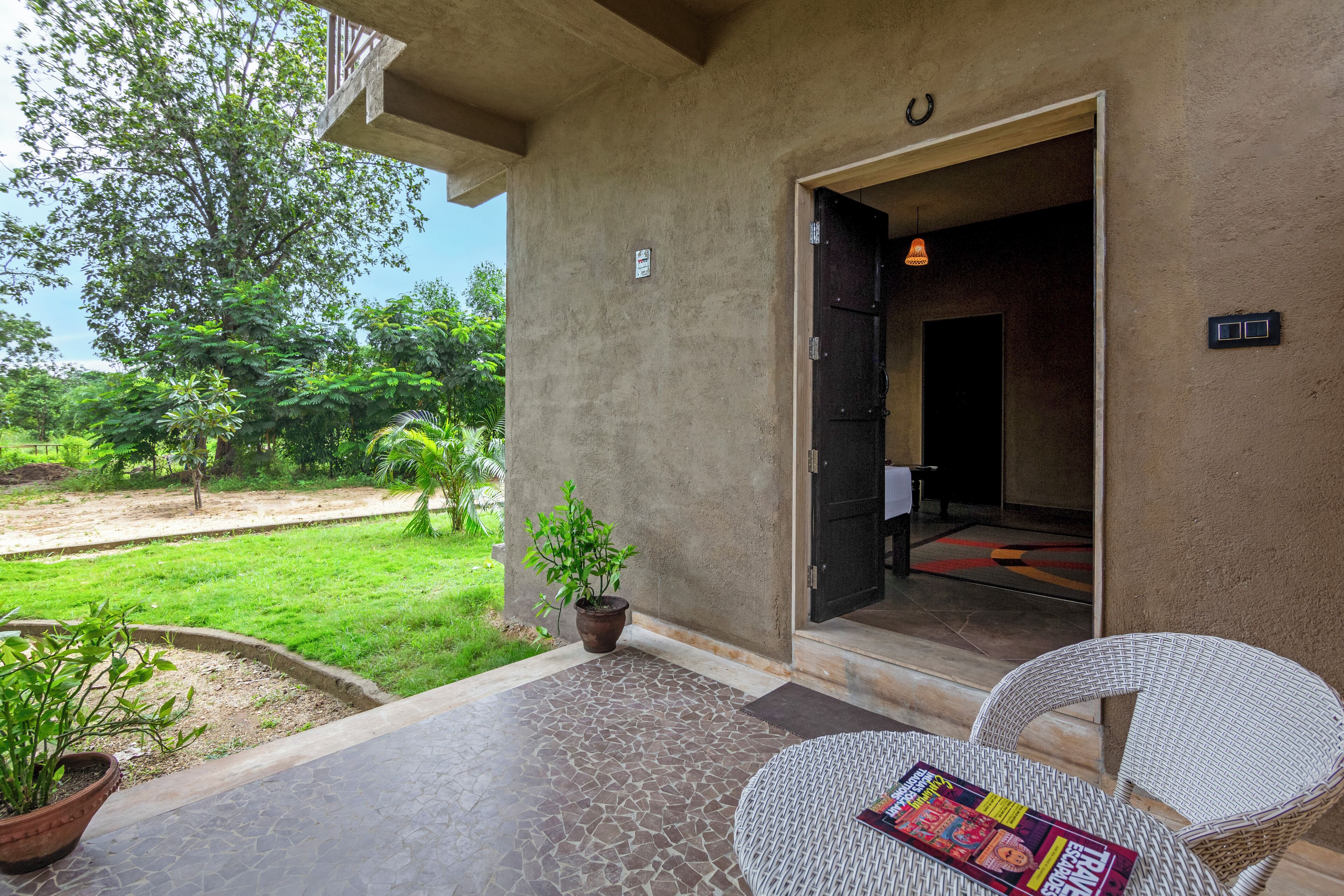 An outdoor area with a tiled floor, a potted plant, and a wicker chair with a magazine.
