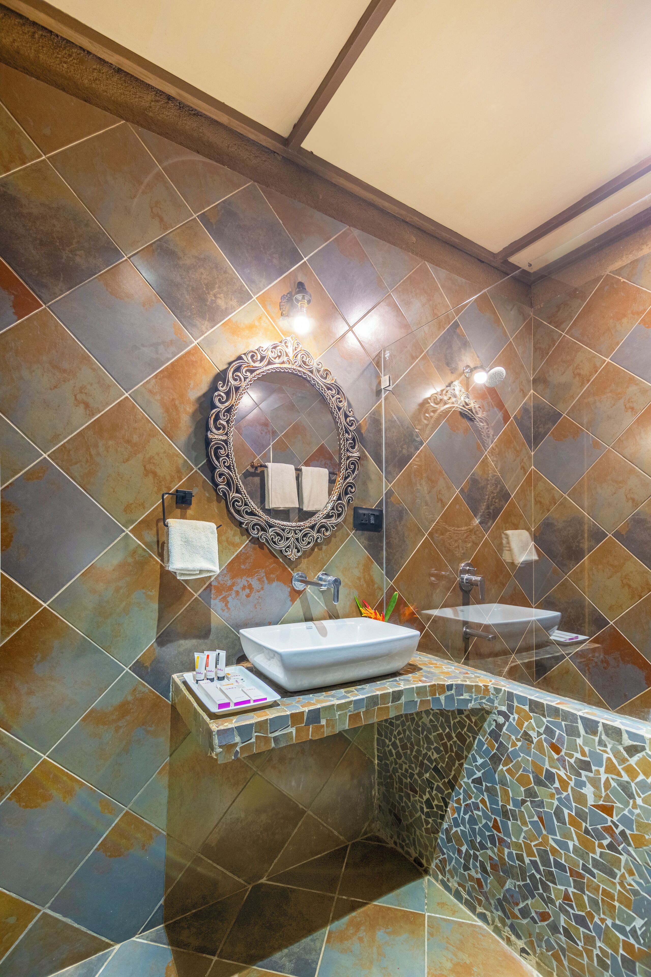 A bathroom with a tiled floor, a sink, a mirror, and a shower.