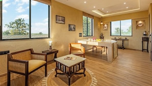 A spacious room with a wooden floor, a dining area with a table and chairs, and large windows offering a view of trees and the sky. - Sterling Orient Woods Pench (Ramtek)