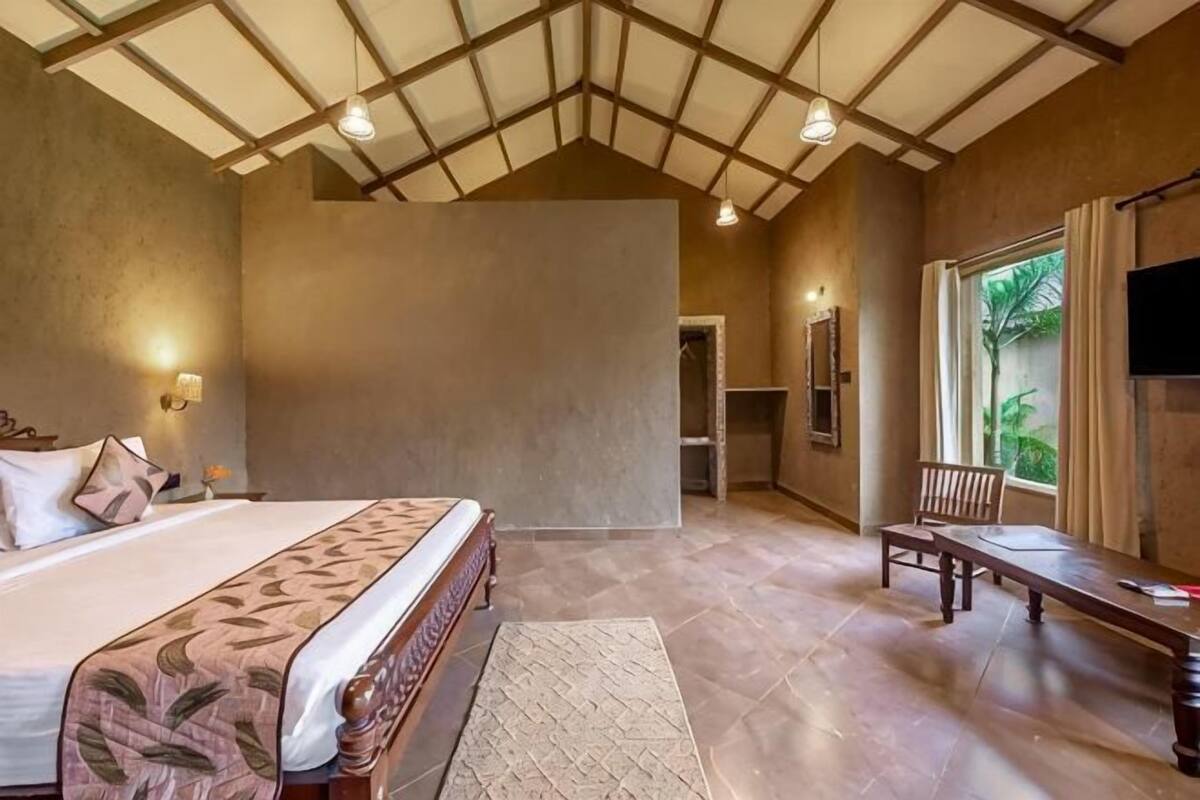 A bedroom with a bed, a bench, a TV, and a window with a view.