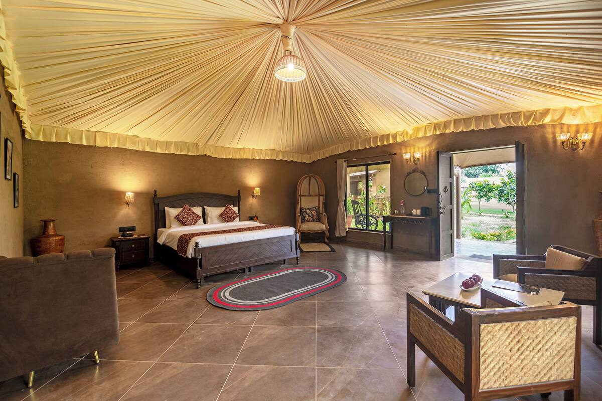 A spacious bedroom with a large bed, a sitting area with a table and chairs, and a view through a glass door to the outdoors.