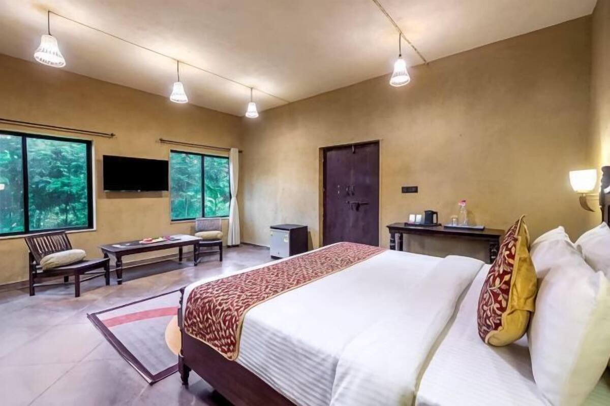 A hotel room with a large bed, a desk, a chair, a TV, and large windows.