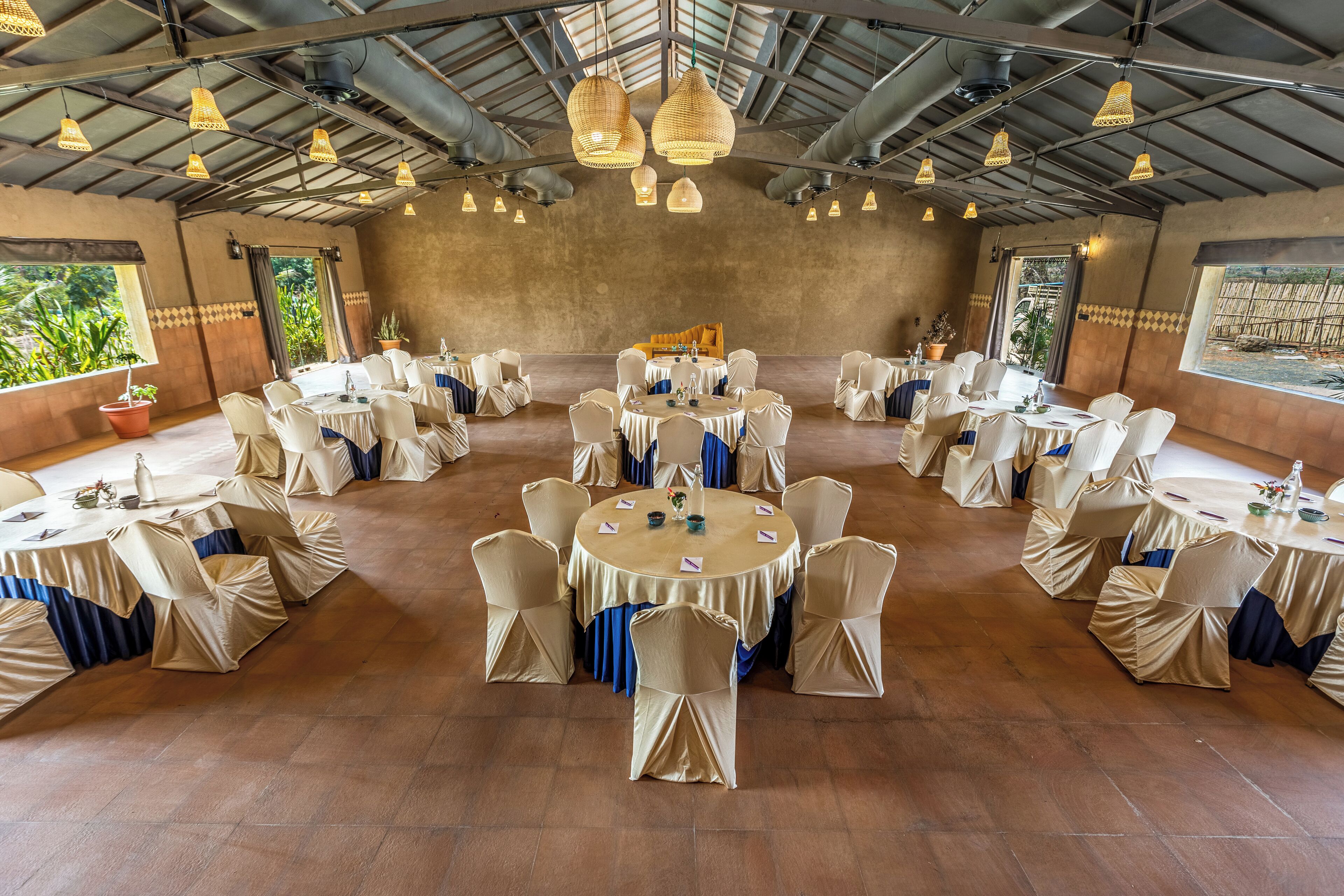 Un salón de banquetes con mesas y sillas redondas, grandes lámparas colgantes y un techo rústico.