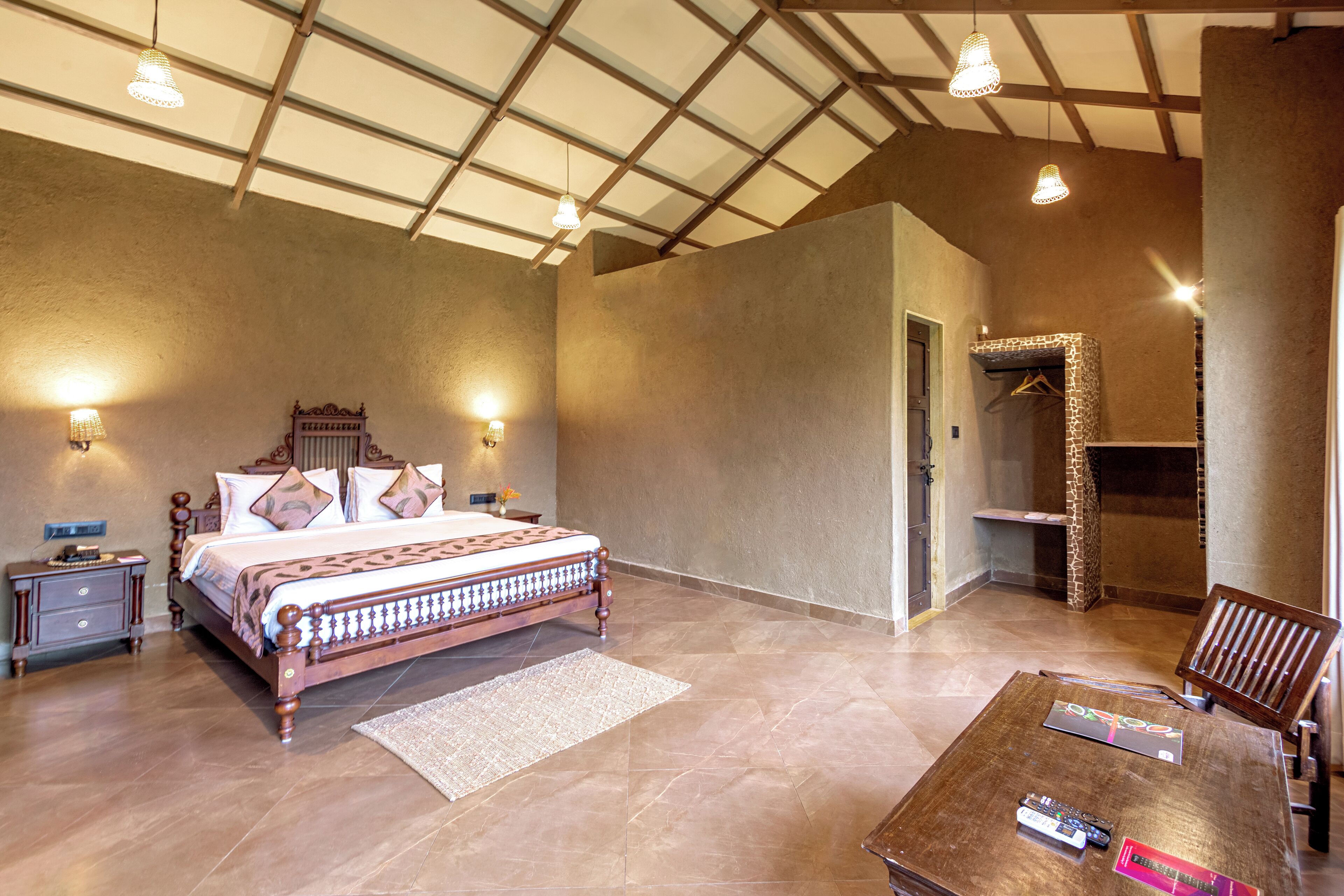 Une chambre spacieuse avec un grand lit, des tables de chevet, une chaise en bois et une petite table sur laquelle se trouvent des livres et une télécommande.