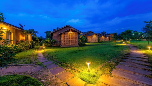 A well-lit courtyard with stone pathways, surrounded by traditional-style buildings with satellite dishes. - Sterling Orient Woods Pench (Ramtek)