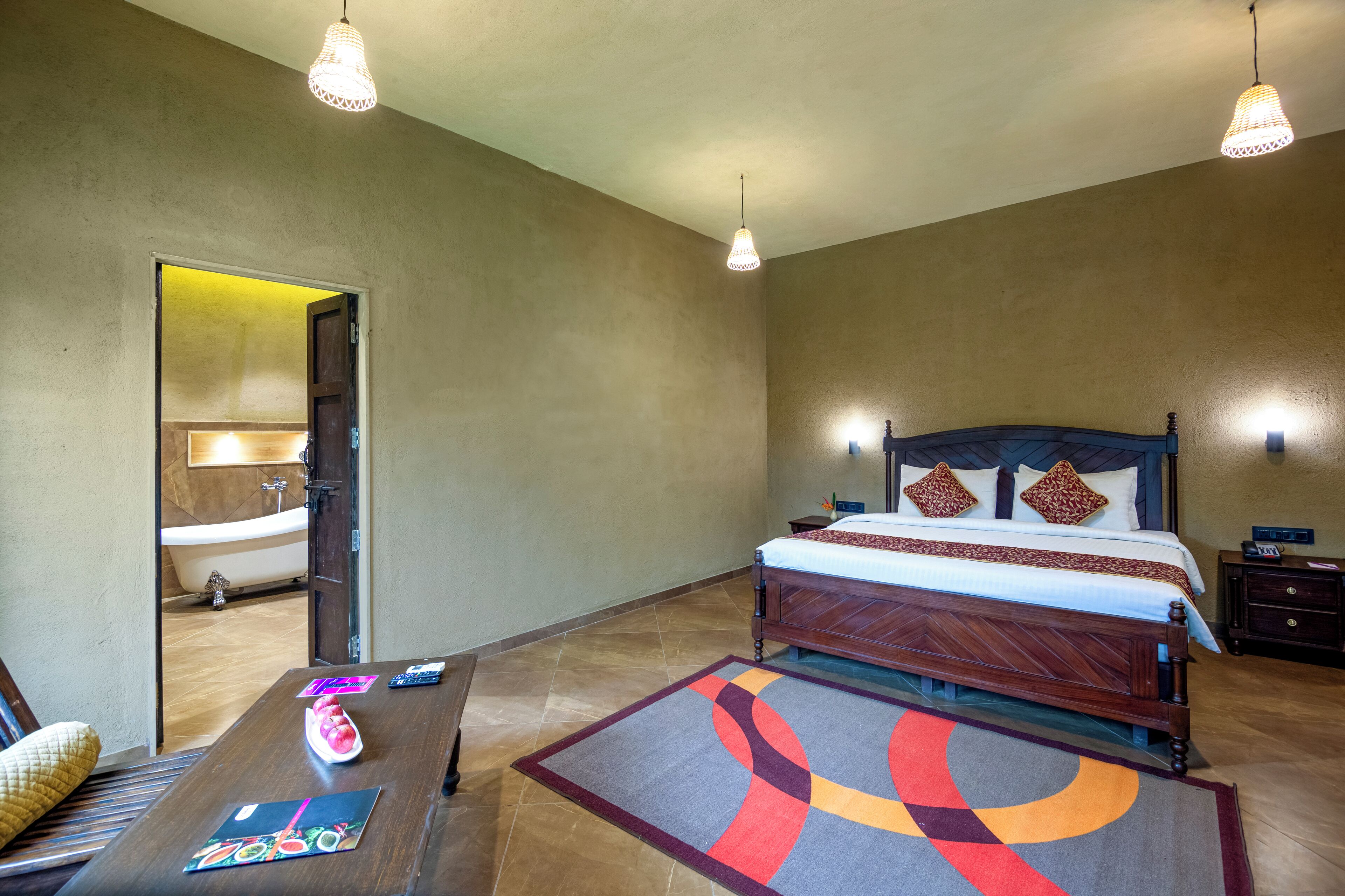 A bedroom with a large bed, bedside tables, a nightstand, a wooden floor, and a bathroom visible through an open door.