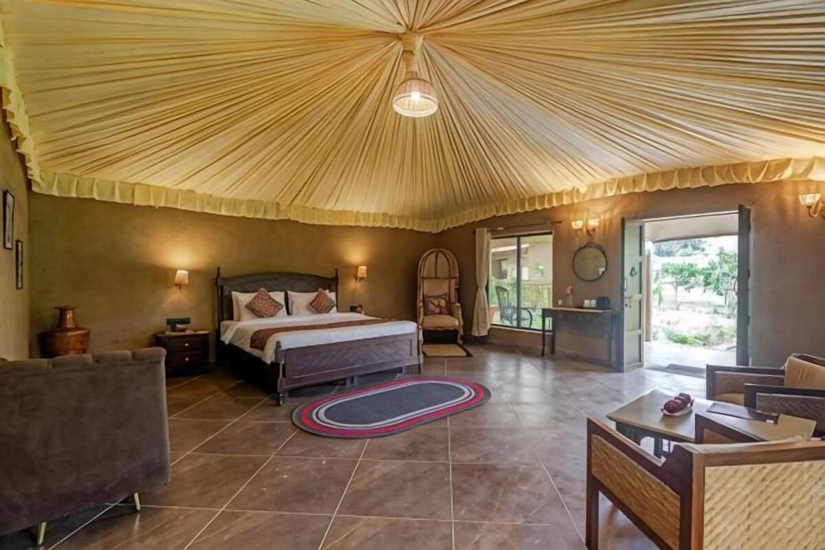 A bedroom with a bed, bedside tables, a chair, a table, and a large umbrella-like ceiling structure.