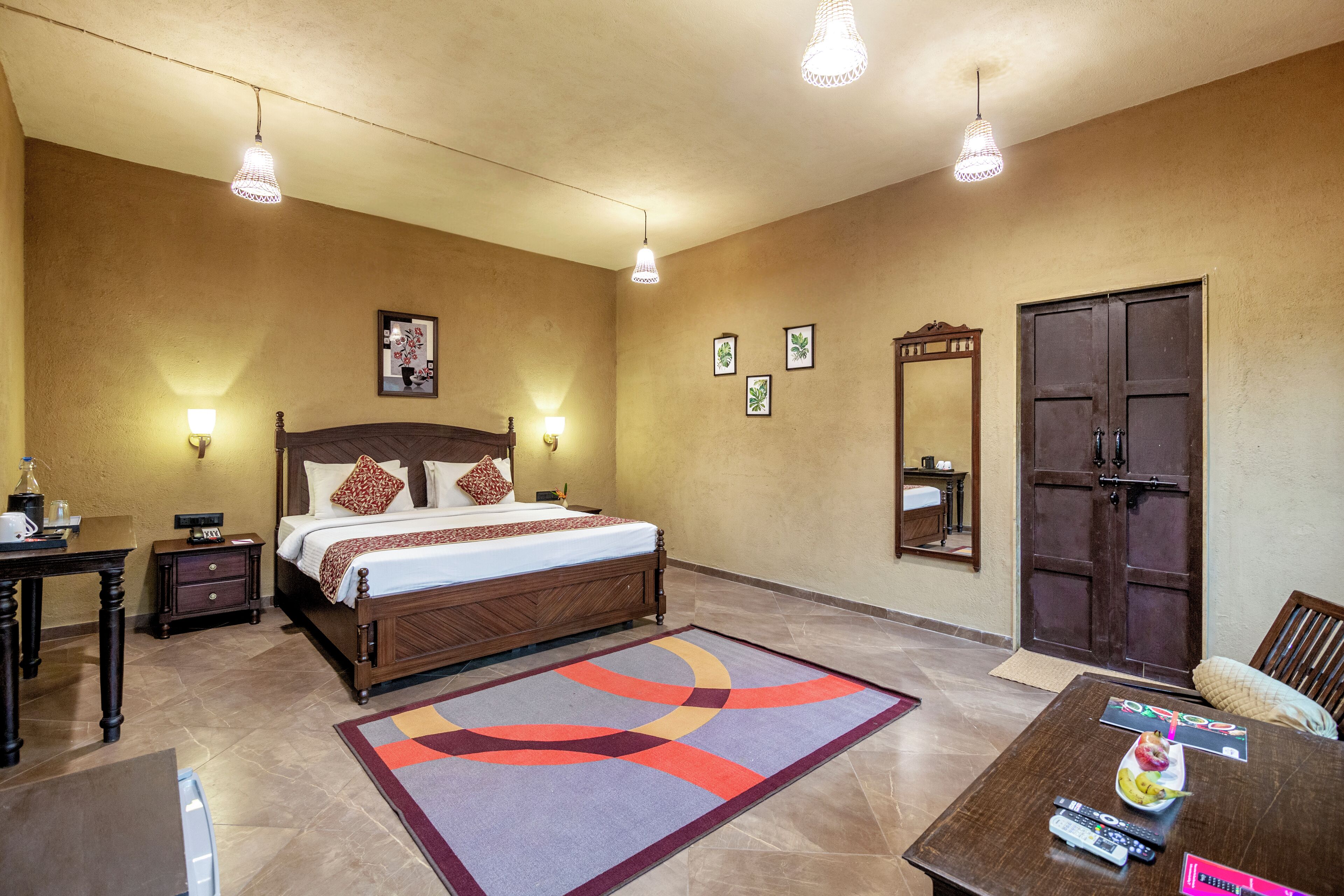 A hotel room with a bed, bedside tables, a desk, a dining table, and a large mirror.