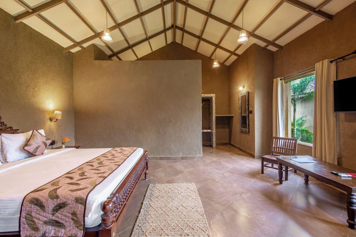 A spacious bedroom with a large bed, a wooden bench, a TV, and a view of the outdoors.