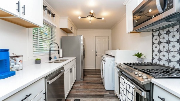 Una cocina compacta con muebles blancos, un refrigerador de acero inoxidable, horno empotrado y microondas.