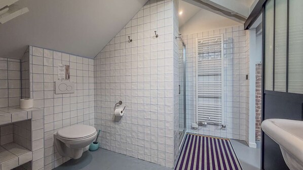 Un baño moderno con paredes de azulejos blancos, inodoro, ducha con puerta de vidrio y una alfombra a rayas.