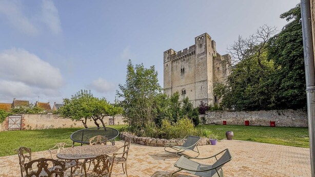 Un patio con una mesa y sillas de piedra, un árbol grande y un castillo al fondo.