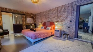 Un dormitorio con una cama grande, una pared de ladrillo, una puerta corredera y una mesita de noche con una lámpara.