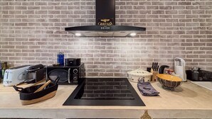 Una cocina con pared de ladrillo, campana extractora negra, tostadora, hervidor y panera.