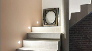 Una escalera con un espejo enmarcado al final, que baja a un nivel inferior con pared de ladrillo.