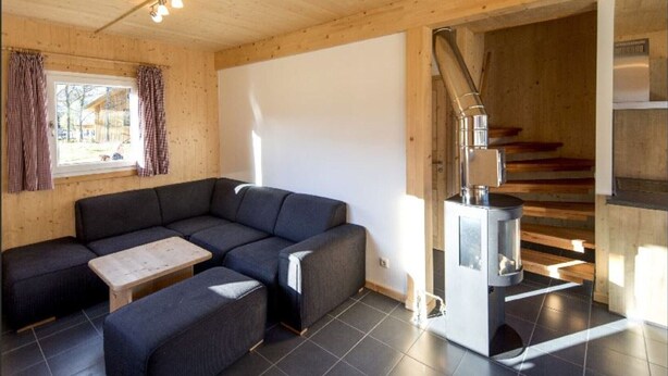 A modern interior with a sectional sofa, a small table, and a wood-burning stove. - Inviting chalet on the ski slopes (Sankt Georgen am Kresichberg)