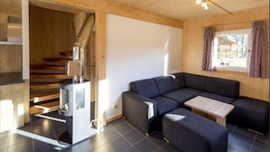 A cozy living room with a sectional sofa, a small wooden table, and a wood-burning stove. - Inviting chalet on the ski slopes (Sankt Georgen am Kresichberg)