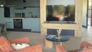 A modern living room with orange armchairs, a coffee table, and a flat-screen TV mounted on a wooden wall. - Luxury private villa with heated pool, spa and sauna (Abreschviller)