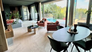 A spacious living area with a pool, modern furniture, and large windows offering a view of the outdoors. - Luxury private villa with heated pool, spa and sauna (Abreschviller)