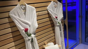 Two white bathrobes with roses tied to wooden hooks on a wall, a wooden bench with a towel, and a wooden bucket. - Luxury private villa with heated pool, spa and sauna (Abreschviller)