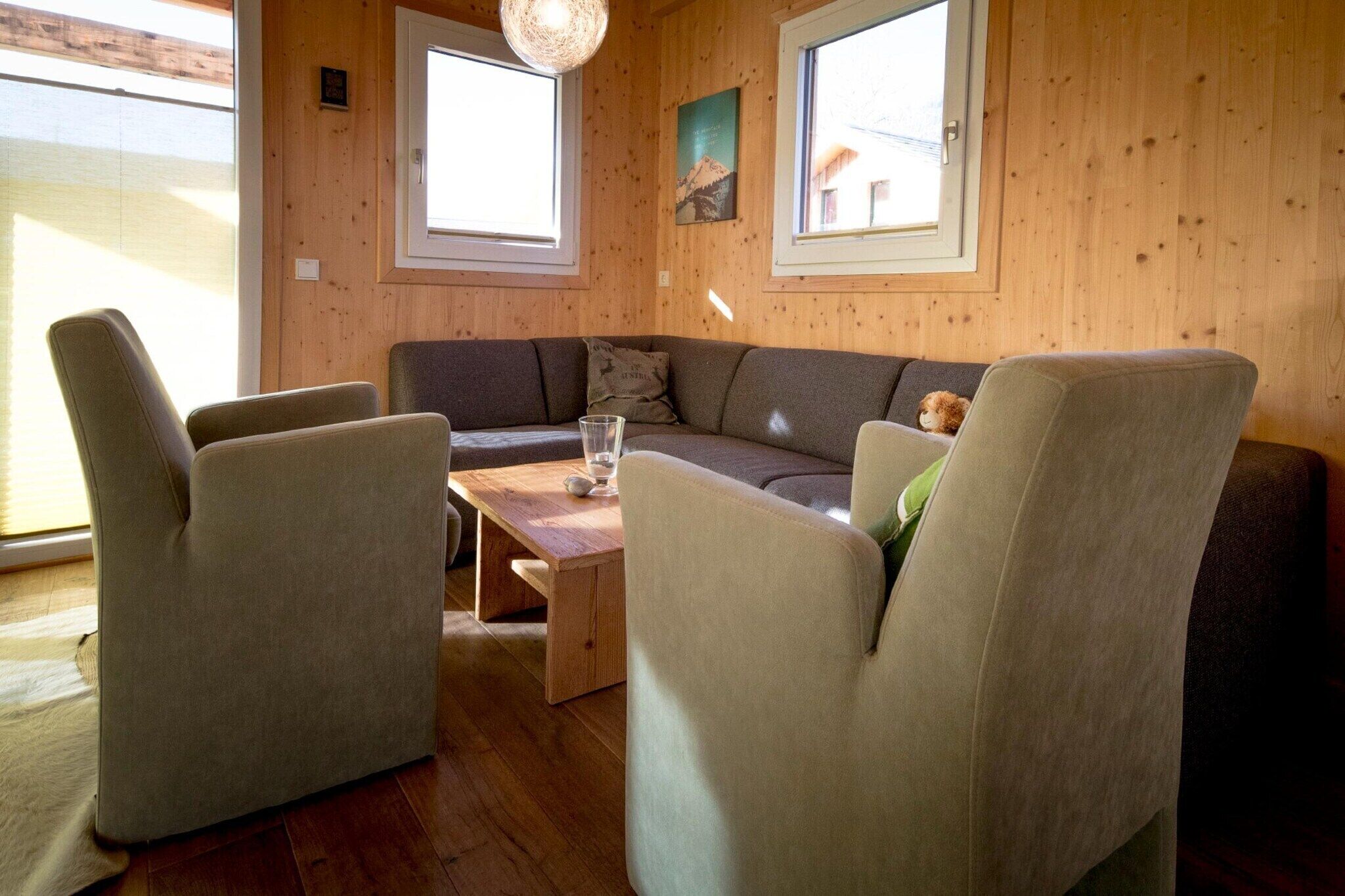 Une pièce chaleureuse avec un décor intérieur en bois, un canapé, deux fauteuils et une petite table avec un plateau en verre.