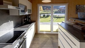A modern kitchen with a built-in stove, microwave, and cabinets, leading to a sliding glass door that opens to a grassy outdoor area. - Amazing chalet with sauna (Sankt Georgen am Kresichberg)