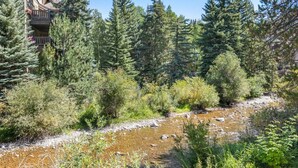 A natural landscape with a stream, dense trees, and a building with balconies. - Vail Village Charm - Walk Everywhere (Vail)