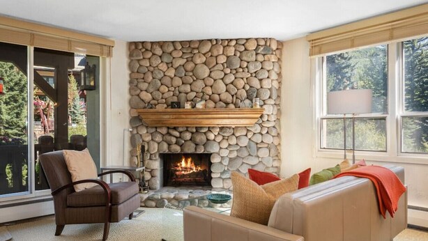 A living room with a stone fireplace, leather sofas, and a large window. - Vail Village Charm - Walk Everywhere (Vail)