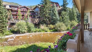 A riverside view with a wooden deck, a river, and buildings with balconies and flower boxes. - Vail Village Charm - Walk Everywhere (Vail)