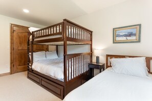A bunk bed with a wooden frame, a bedside table with a lamp, and a single bed with white bedding. - EagleVail Home Near Beaver Creek - Hot Tub & Views (Avon)