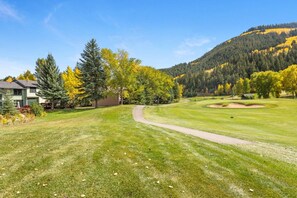 A golf course with a clear path, a building, and a forested hill in the background.