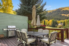An outdoor deck with a grill, dining table, chairs, and a view of a forested hillside. - EagleVail Home Near Beaver Creek - Hot Tub & Views (Avon)