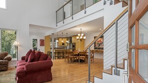 Ampla sala de estar com sofá vermelho, piso de madeira, escada e cozinha ao fundo.