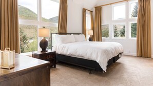Quarto com uma cama grande, duas mesas de cabeceira, cômoda e várias janelas com vista para o exterior.
