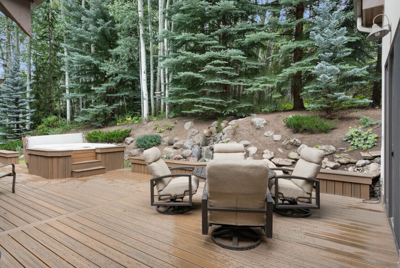 A wooden deck with outdoor seating and a hot tub, surrounded by a forested area.