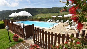 Une piscine bordée de parasols blancs, entourée d’une clôture en bois, et offrant une vue sur un paysage montagneux.