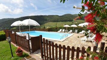 Una piscina con sombrillas blancas, rodeada por una valla de madera, con vistas a un paisaje montañoso.