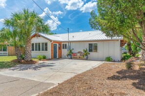 A single-story house with a front porch, a garage, and a small front yard with palm trees and potted plants.