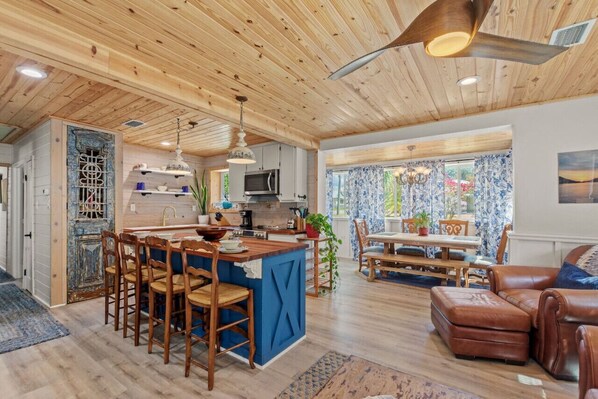 Une cuisine spacieuse avec un plafond en bois, un coin repas avec une table et des chaises, et un salon avec un canapé.