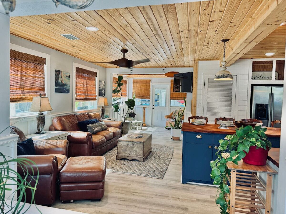 A spacious living room with a leather sofa, a coffee table, and a kitchen area with a blue cabinet and a hanging light fixture.