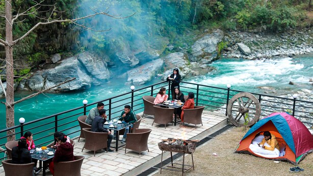 Un espace de restauration au bord de la rivière, avec des tables et des chaises, une tente et un foyer.