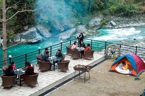 Un espace de restauration au bord de la rivière, avec des tables et des chaises, une tente et un foyer.