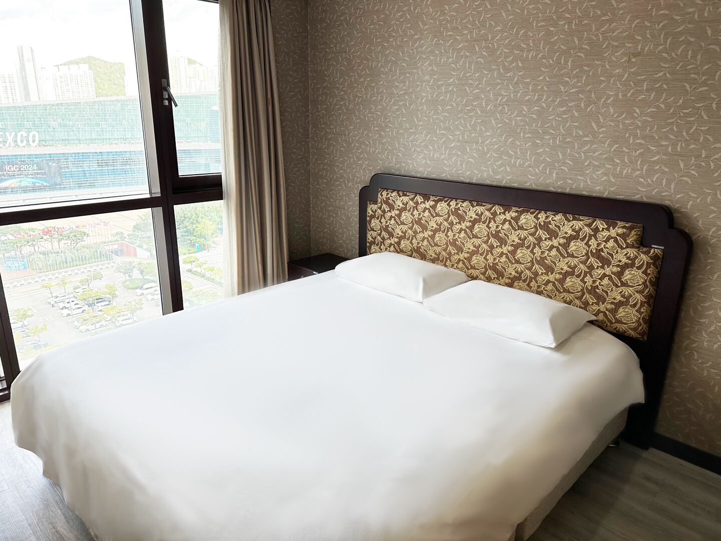 A hotel room with a large bed, a window with curtains, and a patterned headboard.