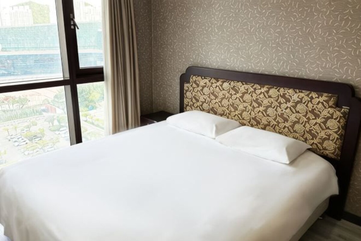 A hotel room with a large bed, a patterned headboard, and a view through a window.