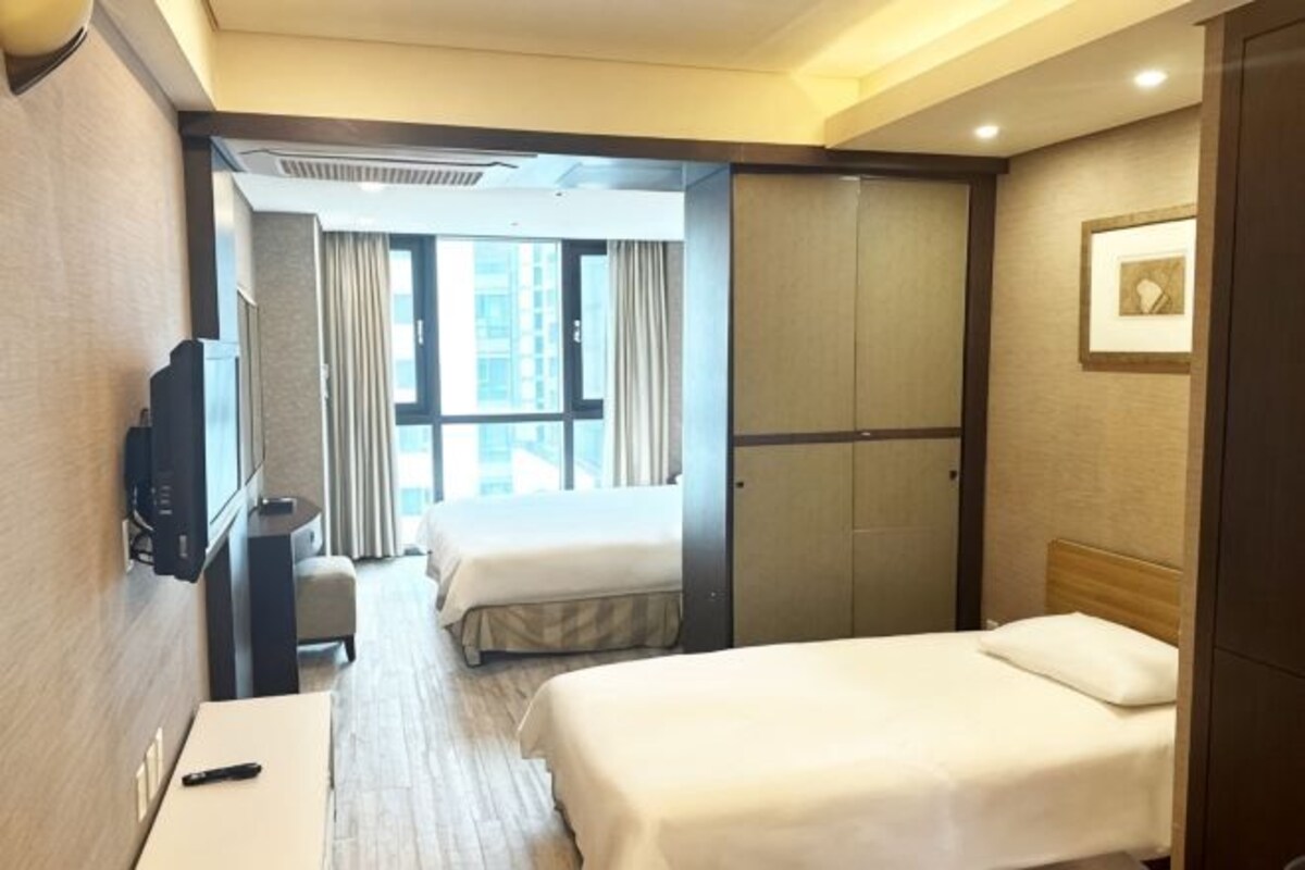 A hotel room with a bed, a desk, a TV, a window, and a door.