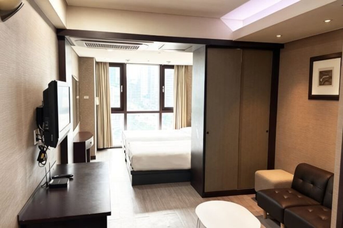 Habitación de hotel con cama, escritorio con televisor, sofá y ventana con cortinas.