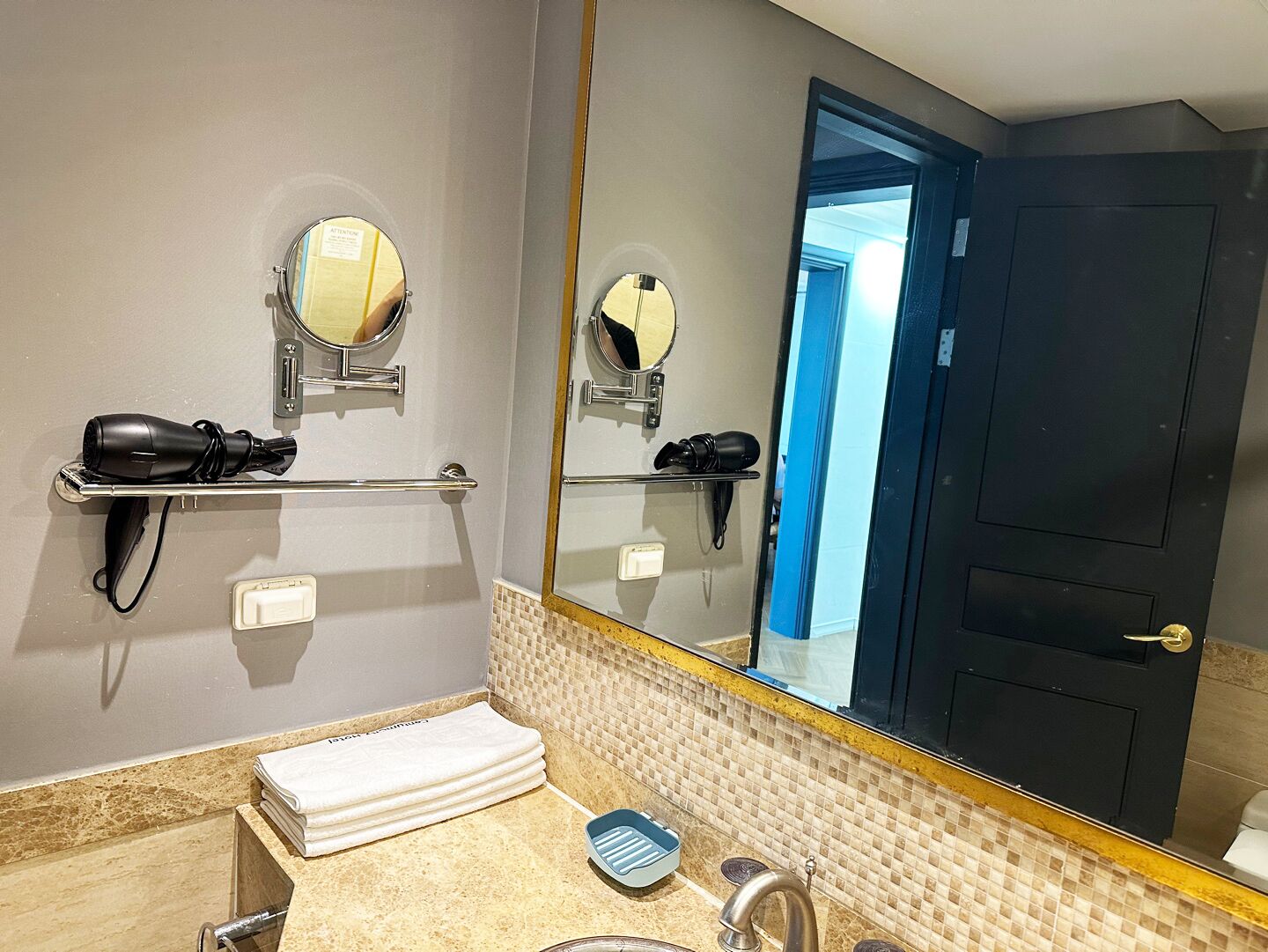 A bathroom with a mirror, towel rack, hairdryer, and a sink.